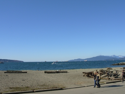 Beachgoers relaxing at English Bay beach with standard city skyline highrises in background