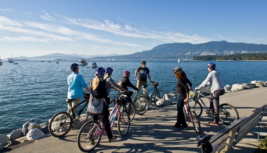 A group of travelers on a guided bicycle tour pause near the seawall path